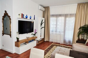Una sala de estar con televisor, libros y objetos decorativos sobre una consola blanca.