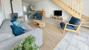 A modern living room with a sofa, chairs, a coffee table, a TV, and a staircase. - Modern House Near Beach: 4 Bedrooms, Full Kitchen, WiFi, Terrace, Parking (Bretignolles-sur-Mer)