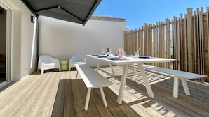 An outdoor patio with a table and chairs, a wooden fence, and a covered area. - Modern House Near Beach: 4 Bedrooms, Full Kitchen, WiFi, Terrace, Parking (Bretignolles-sur-Mer)