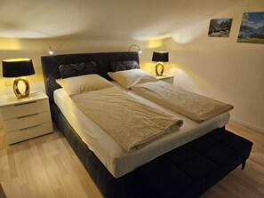 En dubbelsäng med två kuddar, ett sängbord med en lampa och en tavla som hänger på väggen.