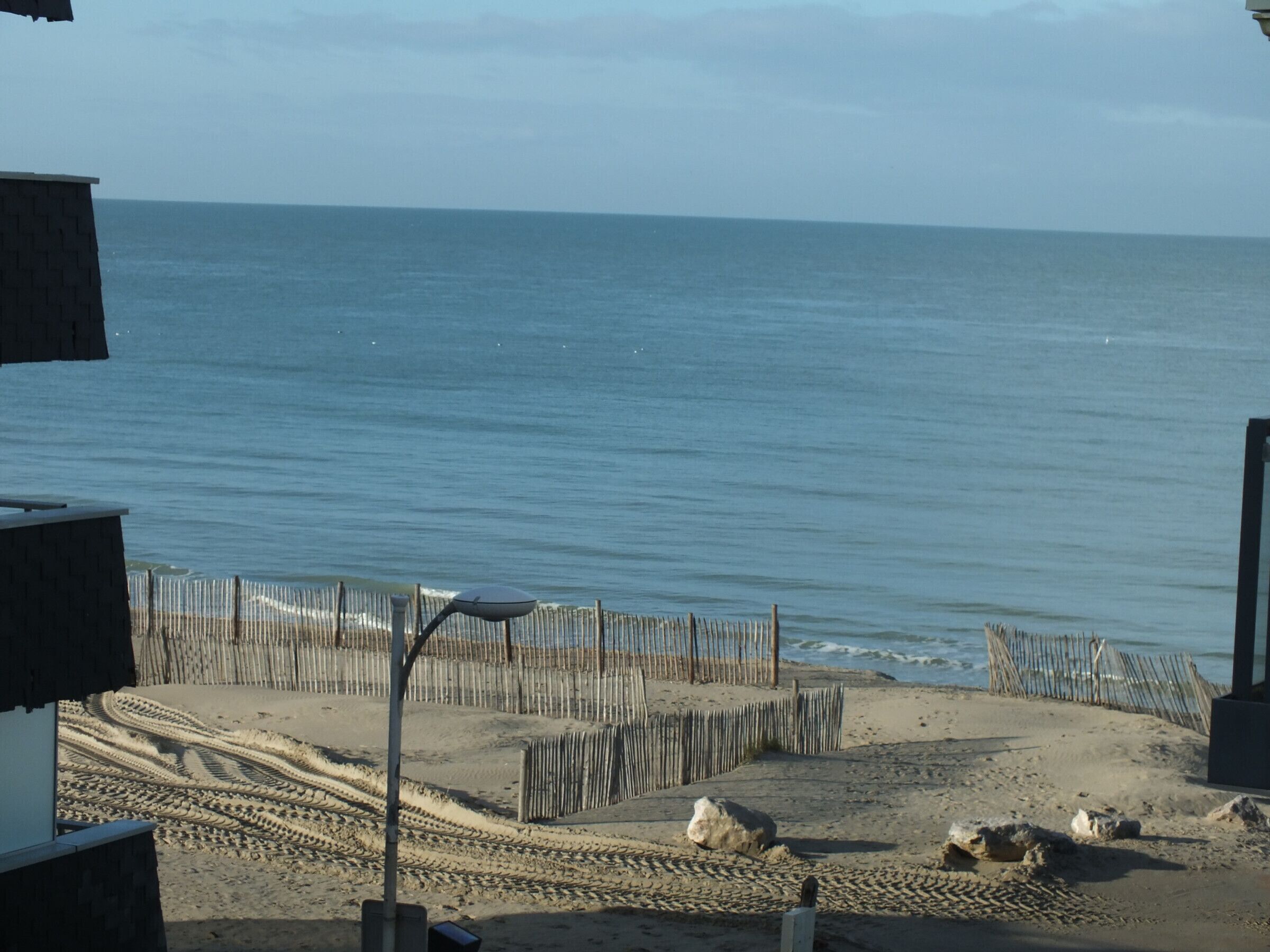 Une plage bordée d’une clôture en bois, avec un chemin pavé et une vue sur l’océan.
