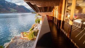 Ein hölzerner Balkon mit einem Steinweg, der zu einer Sitzgelegenheit mit Blick auf einen See und Berge führt.