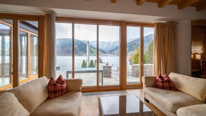 Ein geräumiges Wohnzimmer mit einer großen Schiebeglasdoor, die auf einen Balkon mit Blick auf eine Berglandschaft und ein Gewässer führt.