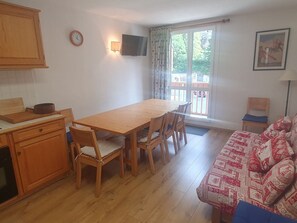 Ein kompakter Wohnraum mit Holztisch, Stühlen, einer Couch, einem Fernseher und einem Fenster mit Vorhängen.
