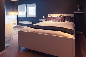 A modern bedroom with a large bed, bedside tables, a chair, and a window with blinds. - SBC Guesthouse (Pajala)