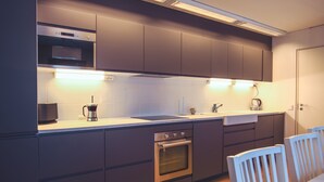 A modern kitchen with dark cabinets, a built-in oven, a microwave, and a coffee maker.