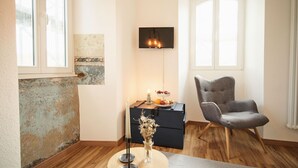 Una sala moderna con piso de madera, un sillón gris, un mueble negro para televisión y una mesita con una vela y flores.