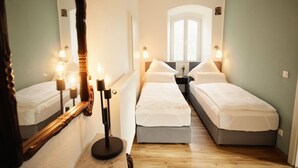 Habitación de hotel con dos camas individuales, un espejo grande, lámparas de noche y vista a la calle por una ventana.