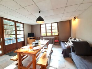 A dining area with a wooden table and benches, a sofa, a TV, and large windows with a view.