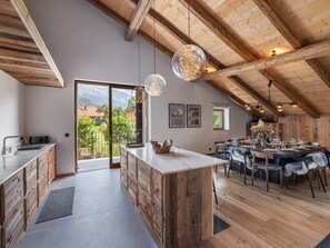 Une cuisine moderne dotée d’un grand îlot central, de poutres en bois et de luminaires suspendus.