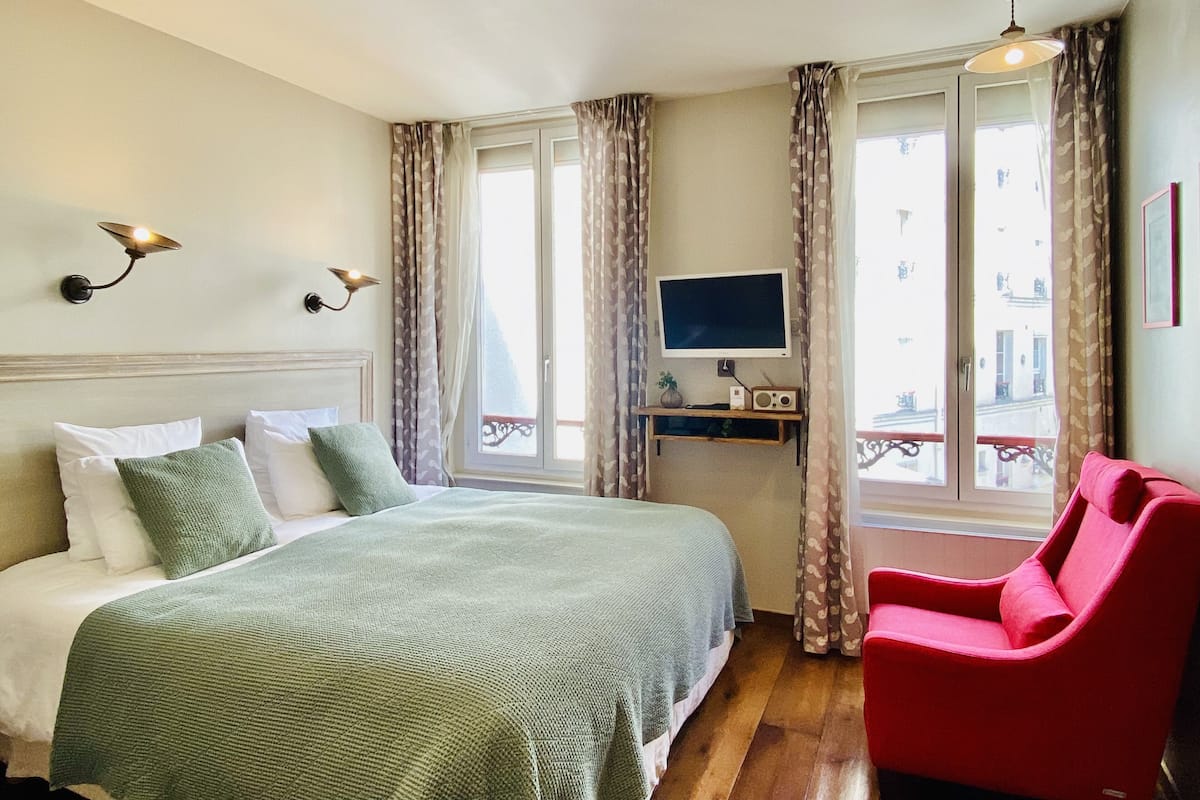 Une chambre d’hôtel avec un lit, une télévision, une radio et un fauteuil rouge.