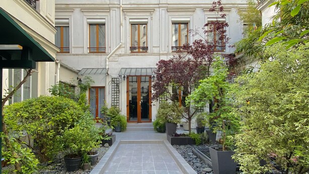 A courtyard with a central pathway, surrounded by potted plants and trees. - CamParis - B&B - Chambre d'hôtes (Paris)