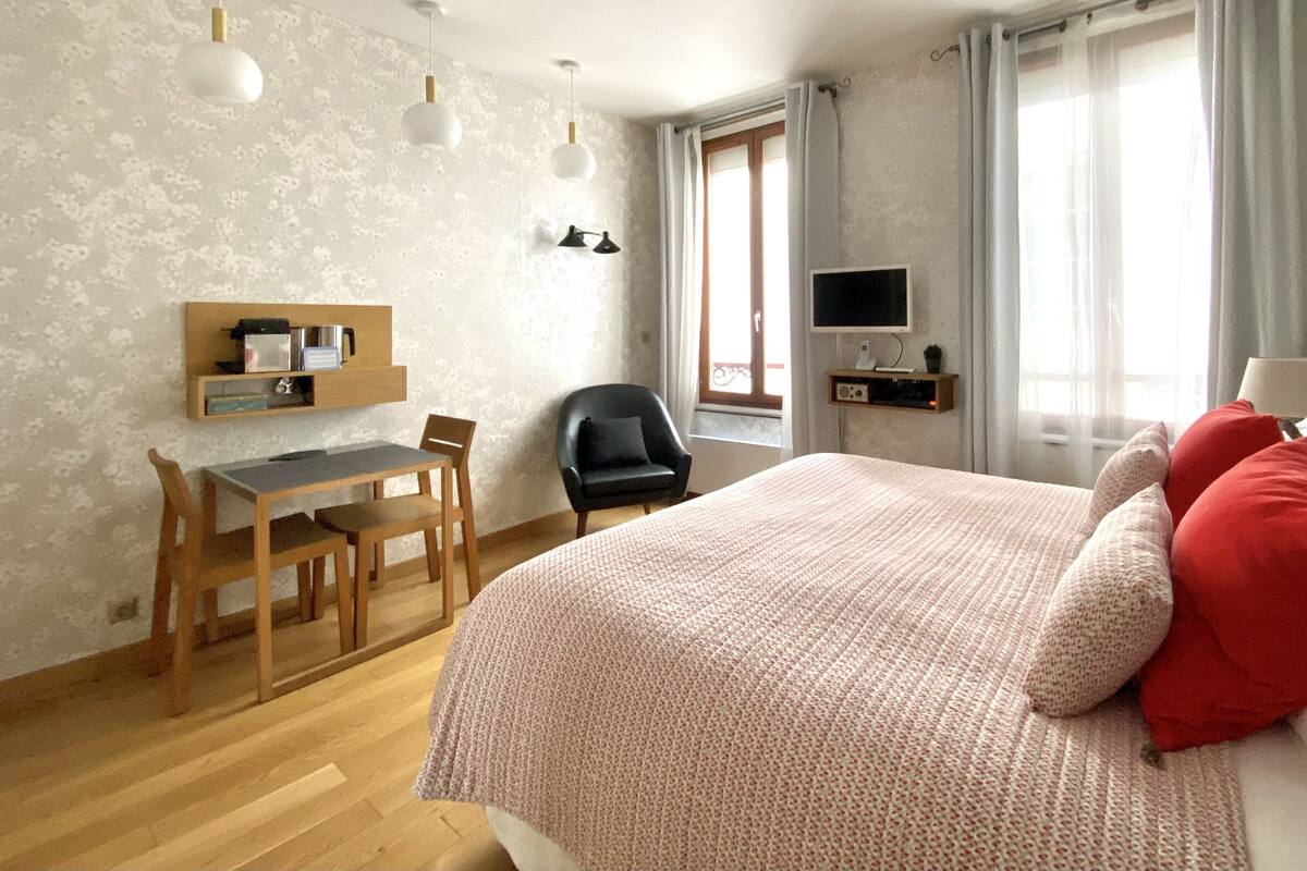 Une chambre à coucher avec un lit, un bureau, une chaise, un téléviseur et une fenêtre avec des rideaux.