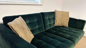 Een donkergroene fluwelen bank met twee beige kussens.