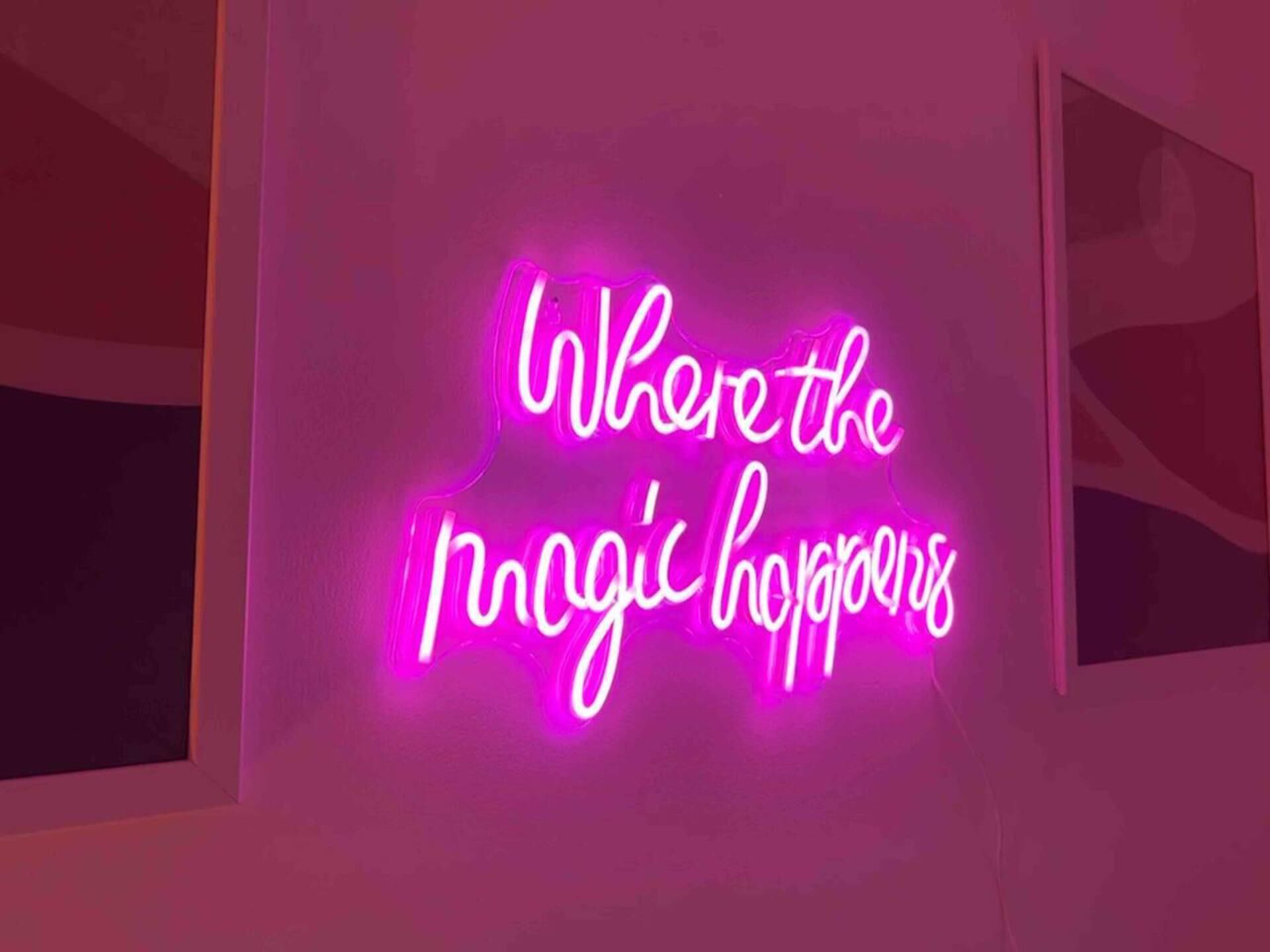 A neon sign with the text "Where the magic happens" on a wall.
