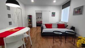Een moderne woonkamer met een bank, twee bijzettafeltjes, een eettafel met stoelen en een rode tafelkleed.