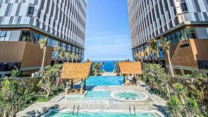 Ein modernes Hotel mit zentralem Pool, umgeben von Palmen und freiem Blick auf den Ozean.