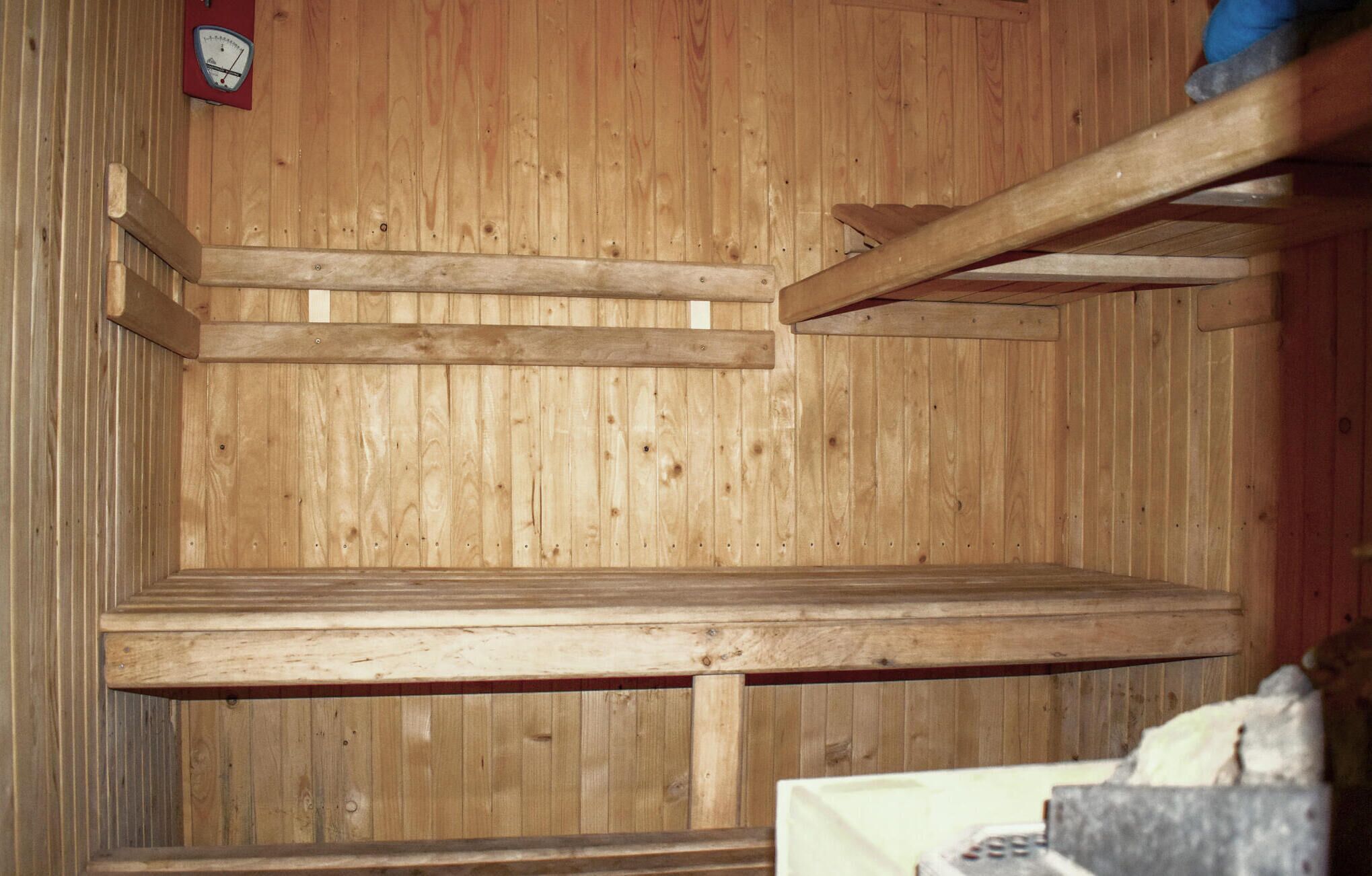 A wooden interior with a wooden bench and a wall-mounted thermometer.