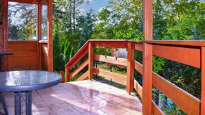 Un terrazzo in legno con tavolo e panche in metallo, immerso nel verde e alberi.