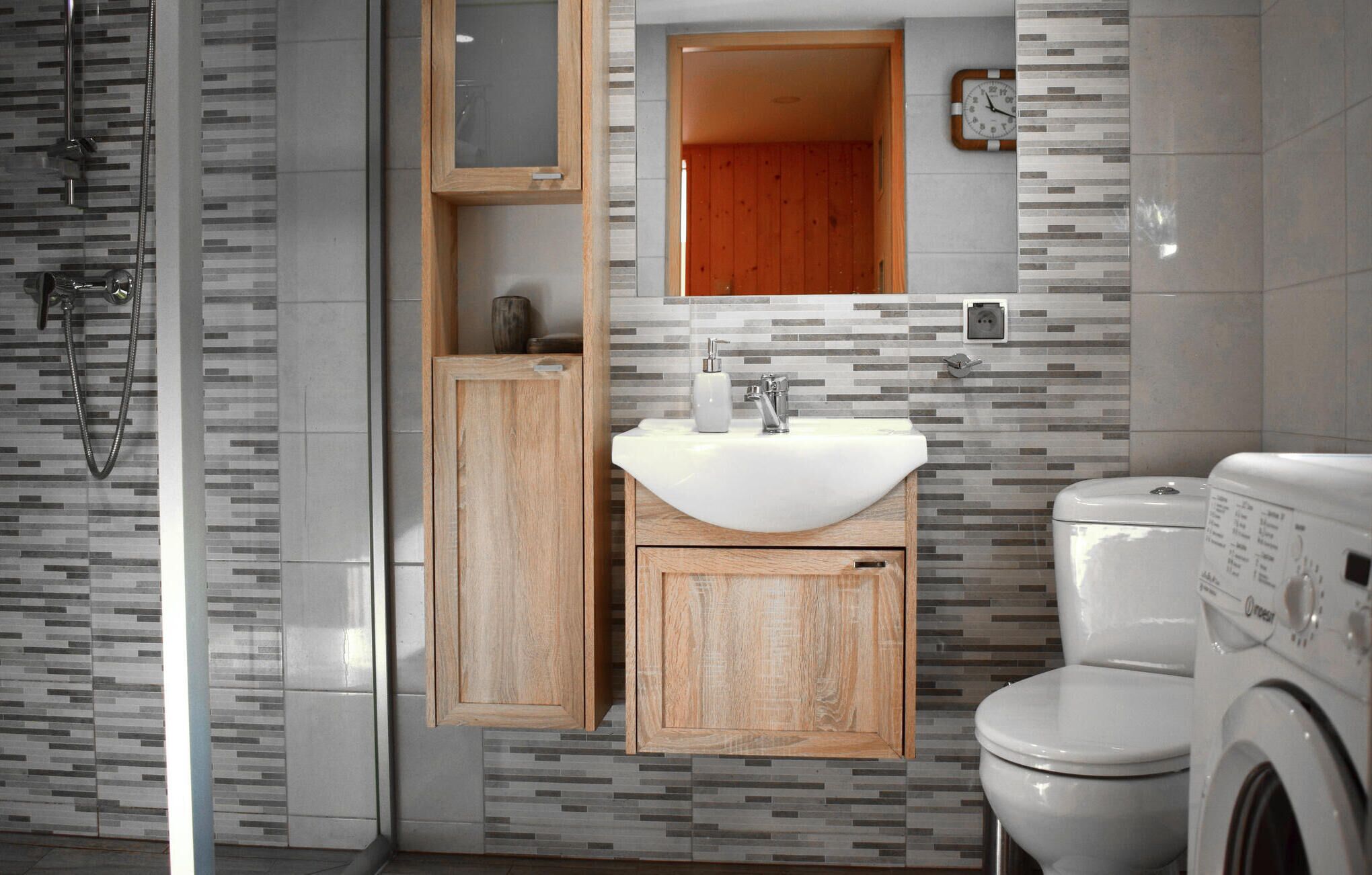 A modern bathroom with a wooden vanity, a sink, a toilet, and a washing machine.