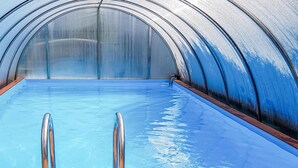 Una piscina interna con acqua cristallina, scalette metalliche e una struttura del soffitto curva.