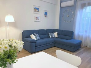 Un salon avec un canapé bleu, une table blanche et une horloge au mur.