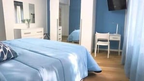 Ein Schlafzimmer mit Bett, Schreibtisch, Stuhl, Fernseher und Spiegel.
