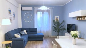 Ein modernes Wohnzimmer mit einem blauen Sofa, einem Esstisch und einem Fernseher.
