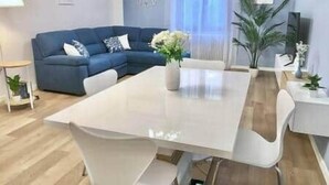 Ein modernes Wohnzimmer mit einem blauen Sofa, einem weißen Esstisch und einem Blumentopf.