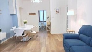 Ein modernes Wohnzimmer mit einem blauen Sofa, einem Esstisch mit Stühlen und einer Küchenzeile im Hintergrund.