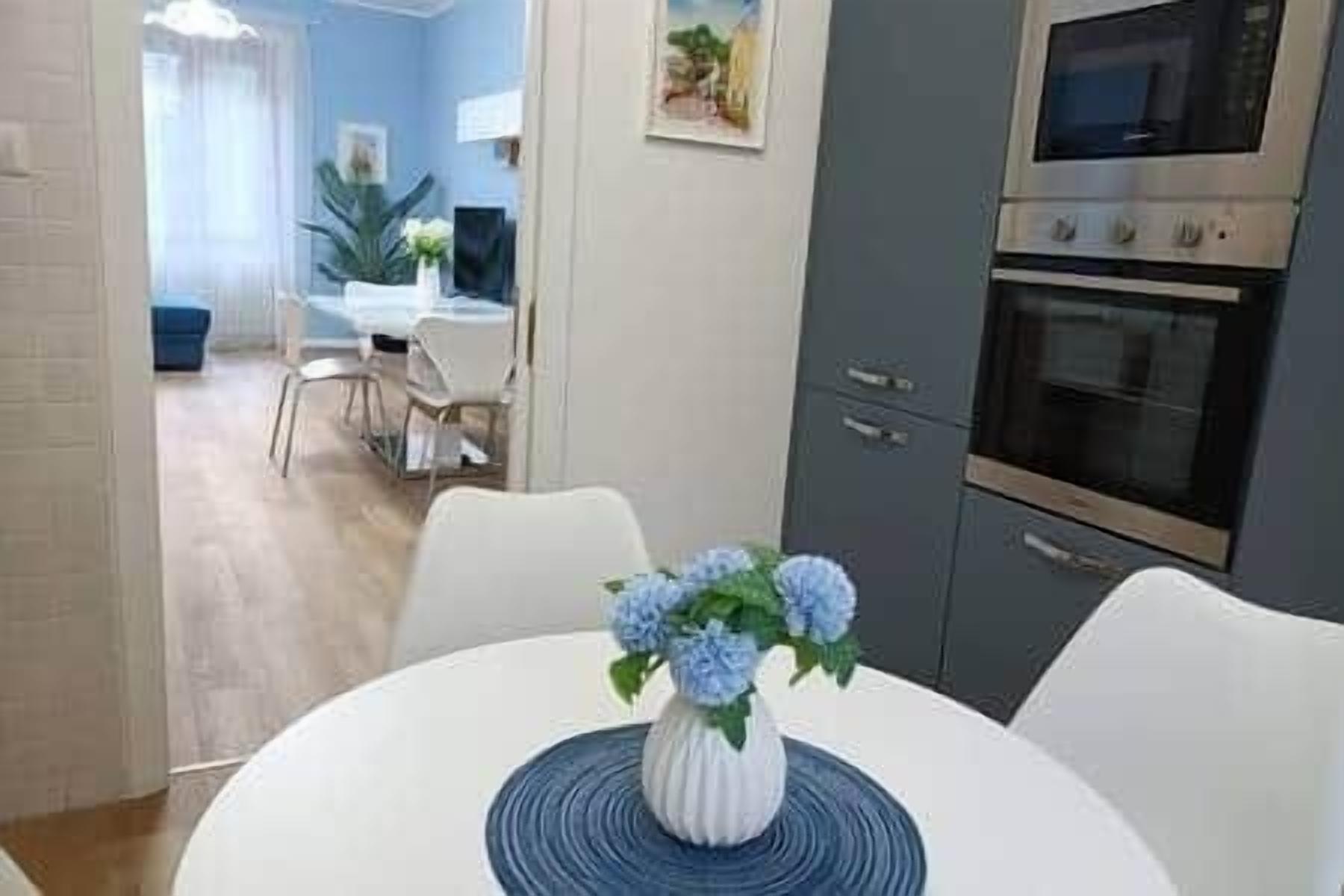 A dining area with a white table, blue flowers, and a view into a living room with a blue sofa and a plant.