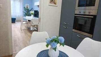 A dining area with a white table, blue flowers, and a view into a living room with a blue sofa and a plant.