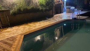 Une piscine dotée d’une terrasse en bois, entourée d’un mur de pierre orné de plantes grimpantes.