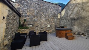 Un bâtiment en pierre doté d’une terrasse en bois, d’un espace salon extérieur et d’un jacuzzi.