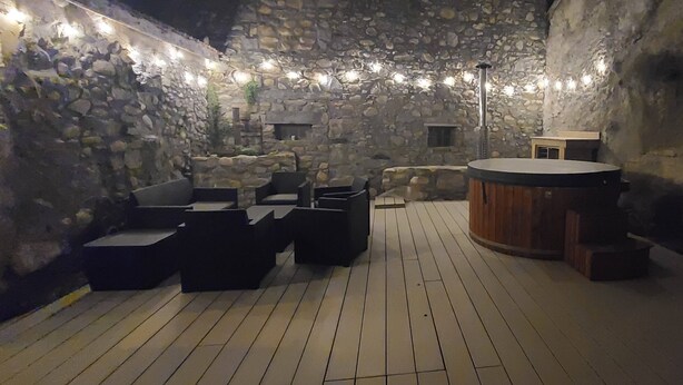 Un espace extérieur aménagé avec des murs en pierre et un sol en bois, comprenant un jacuzzi et divers types de sièges.
