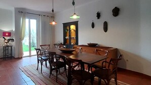 Un comedor amplio con una gran mesa de madera y sillas, una alfombra estampada e iluminación colgante.