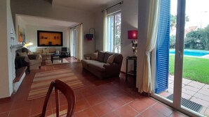 Amplia sala de estar con sofá, sillones y televisión. Posee un ventanal corredizo que da a un balcón con piscina.