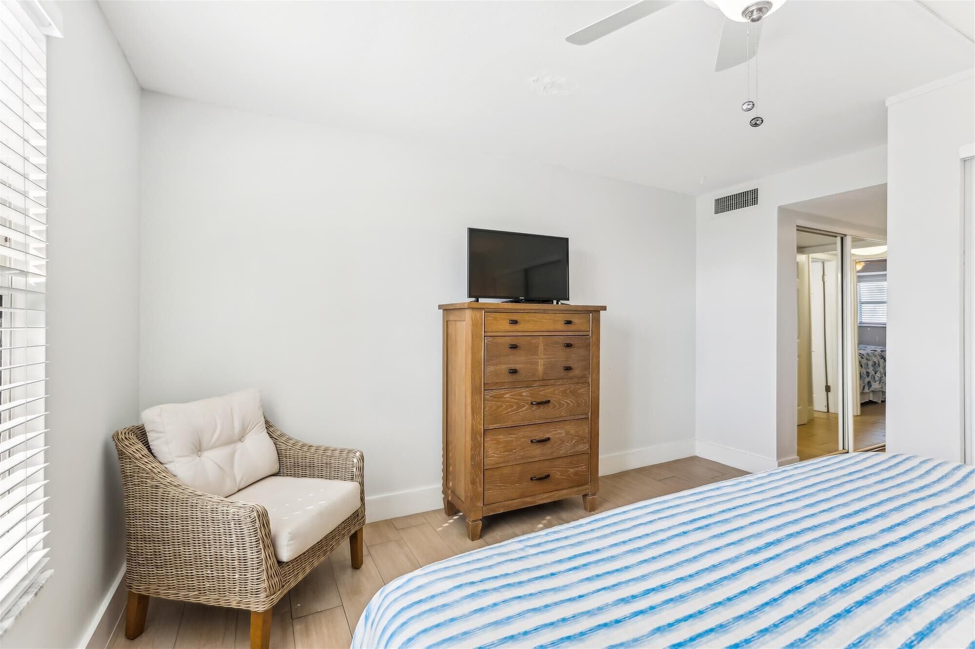 A bedroom with a bed, a wicker chair, a wooden dresser, and a television on top.