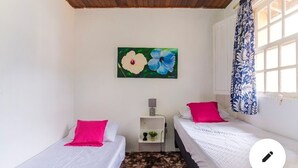 Ein Zimmer mit zwei Betten, einem kleinen Nachttisch, einem Blumenbild und einem Fenster mit Vorhang.