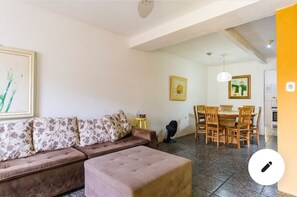 A living room with a sofa, a dining table with chairs, and a fan.