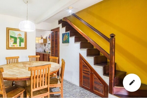 A dining area with a wooden table and chairs, a staircase with wooden railings, and artwork on the walls.
