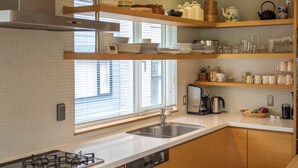 A modern kitchen with a gas stove, dishwasher, and a window with blinds. - Chalet Murasaki (Kutchan)
