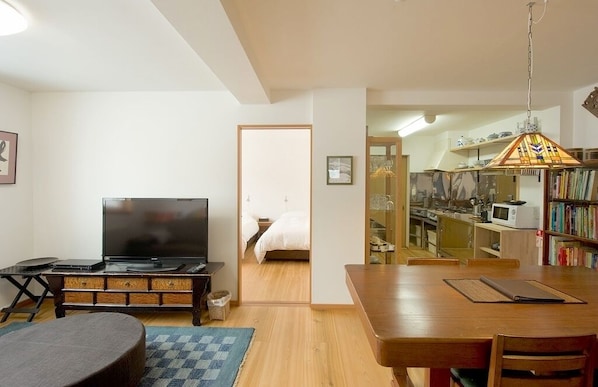 A living room with a TV, a dining table, and a kitchen area visible through an open doorway. - Chalet Murasaki (Kutchan)