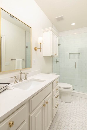A bathroom with a white vanity, a large mirror, a toilet, and a shower area.
