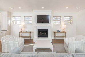 A living room with a fireplace, two armchairs, a coffee table, and a TV mounted above the fireplace. - The Douglas: Luxury Home Steps from Dickson & UoA (Fayetteville)