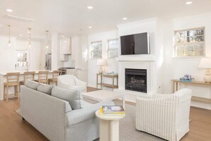 A modern living room with a sofa, armchairs, a fireplace, a television, and a kitchen area with bar stools.