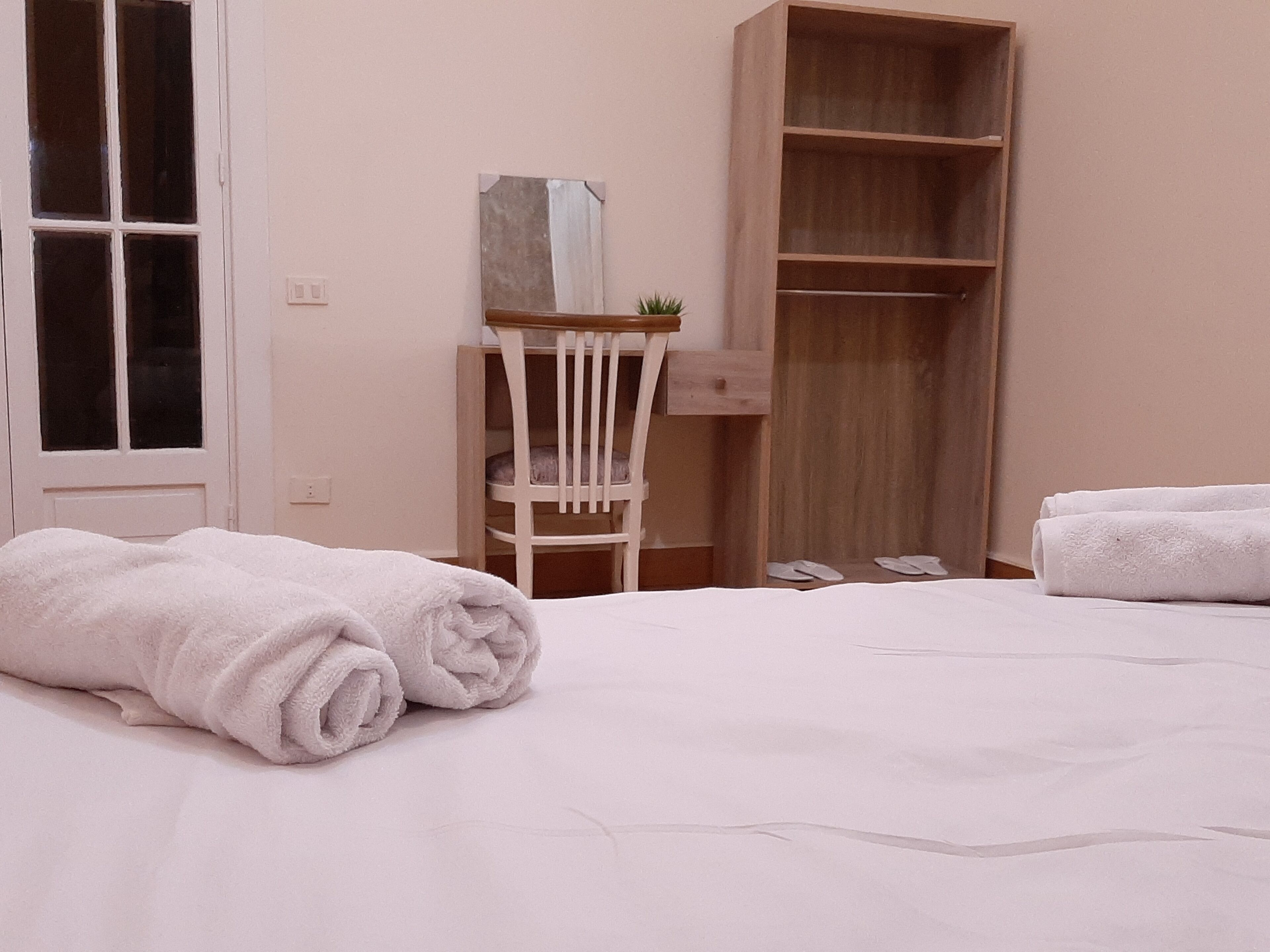A bedroom with a bed, a wooden wardrobe, a white chair, and a small table with a plant.