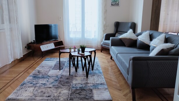 A living room with a sofa, a coffee table, a TV, and a window with curtains. - Royal Apartment in Talaat Harb Downtown  (Cairo)