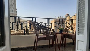 A balcony with two wicker chairs and a small table, a potted plant, and a view of buildings in the background. - Royal Apartment in Talaat Harb Downtown  (Cairo)