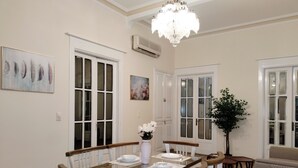 A dining area with a glass-top table, white chairs, a chandelier, and a potted plant. - Royal Apartment in Talaat Harb Downtown  (Cairo)